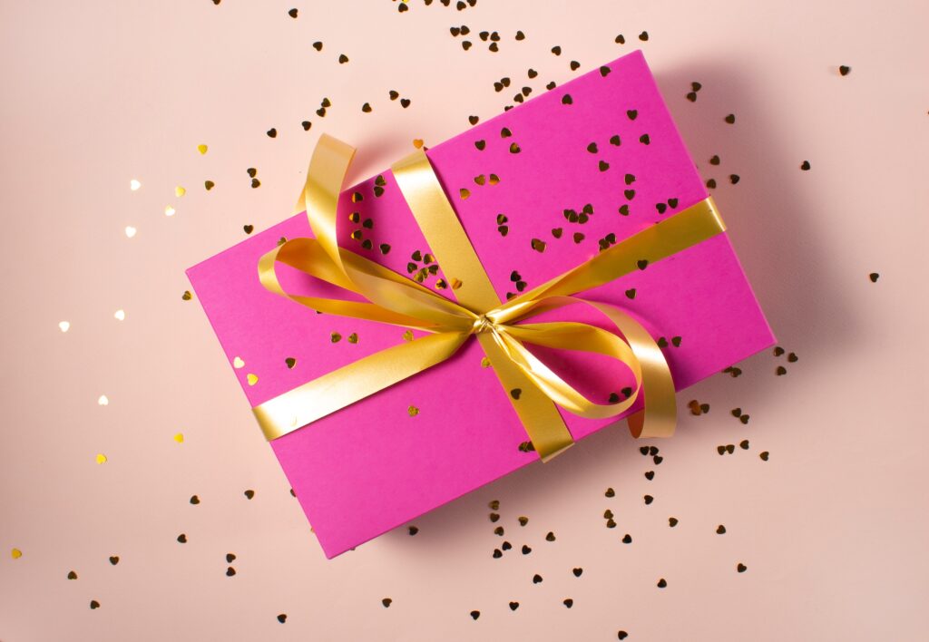 Geschenkgutschein in rosafarbener Verpackung mit goldener Schleife und Konfetti in Herzform