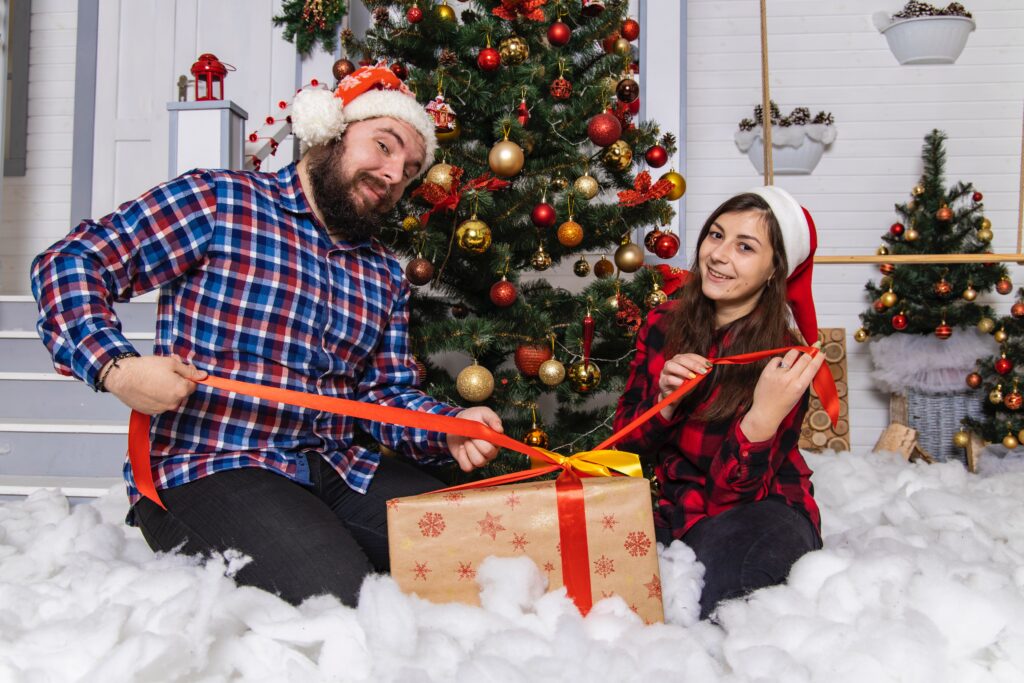 Ein Mitarbeiter und eine Mitarbeiterin sitzen vor dem Weihnachtsbaum und packen gespannt ihr Weihnachtsgeschenk aus